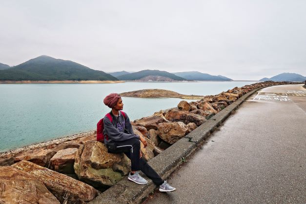 Woman sits on wall near a river. 