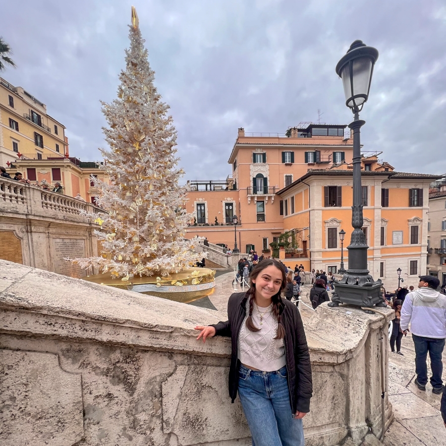 student stands in front of a fir tree in a European city